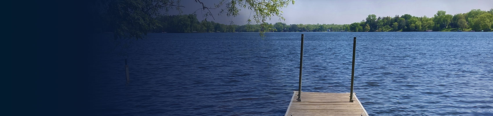 the end of a dock extending into a lake with trees in the distance